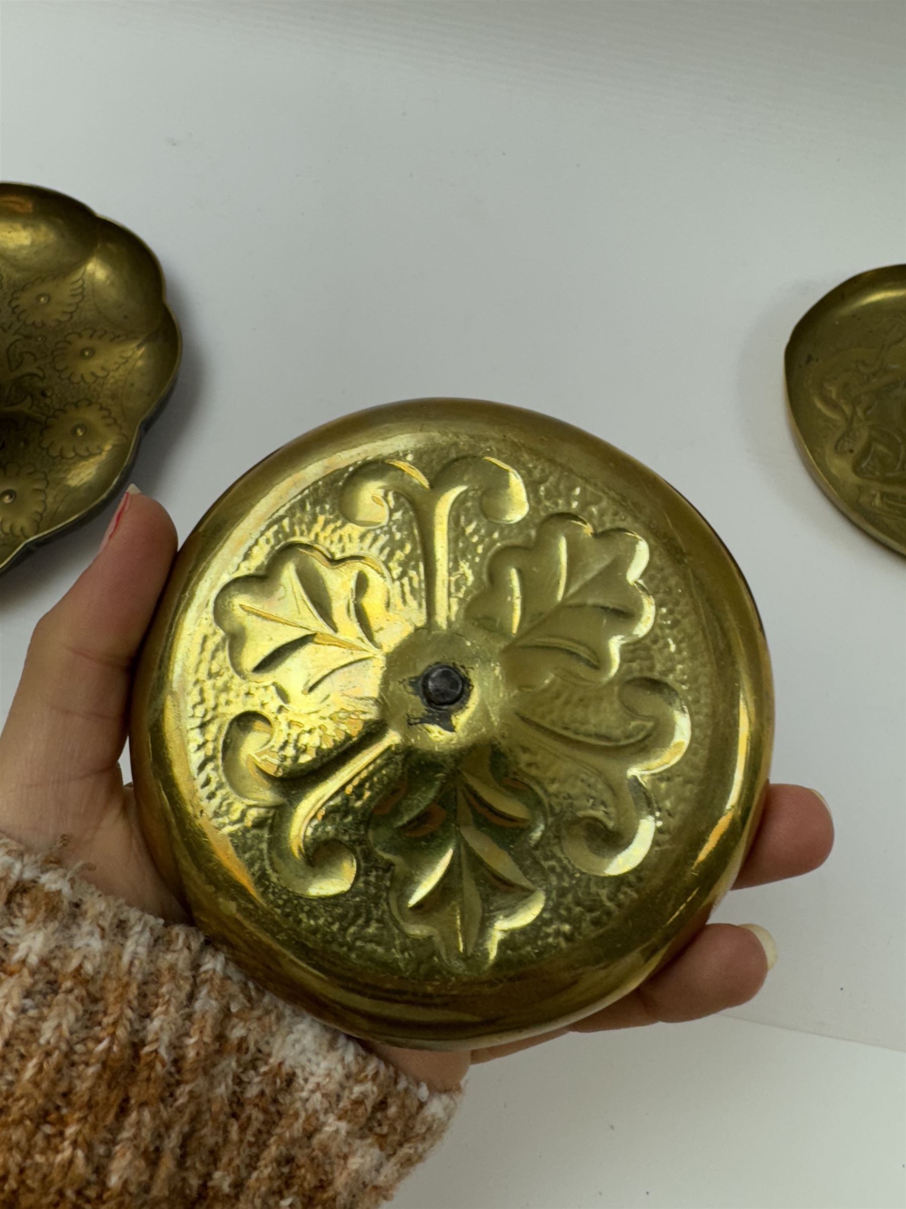 Three Arts & Crafts brass chambersticks/candlesticks, to include a small Keswick School of Industrial Arts example, with repousse leaf decoration, stamped KSIA, a chamberstick with Art Nouveau style decoration to drip pan and blue enamel roundel inset into the loop handle and a larger candlestick, with shaped rim and sconce, repousse decoration and lightly hammered finish, largest D18cm