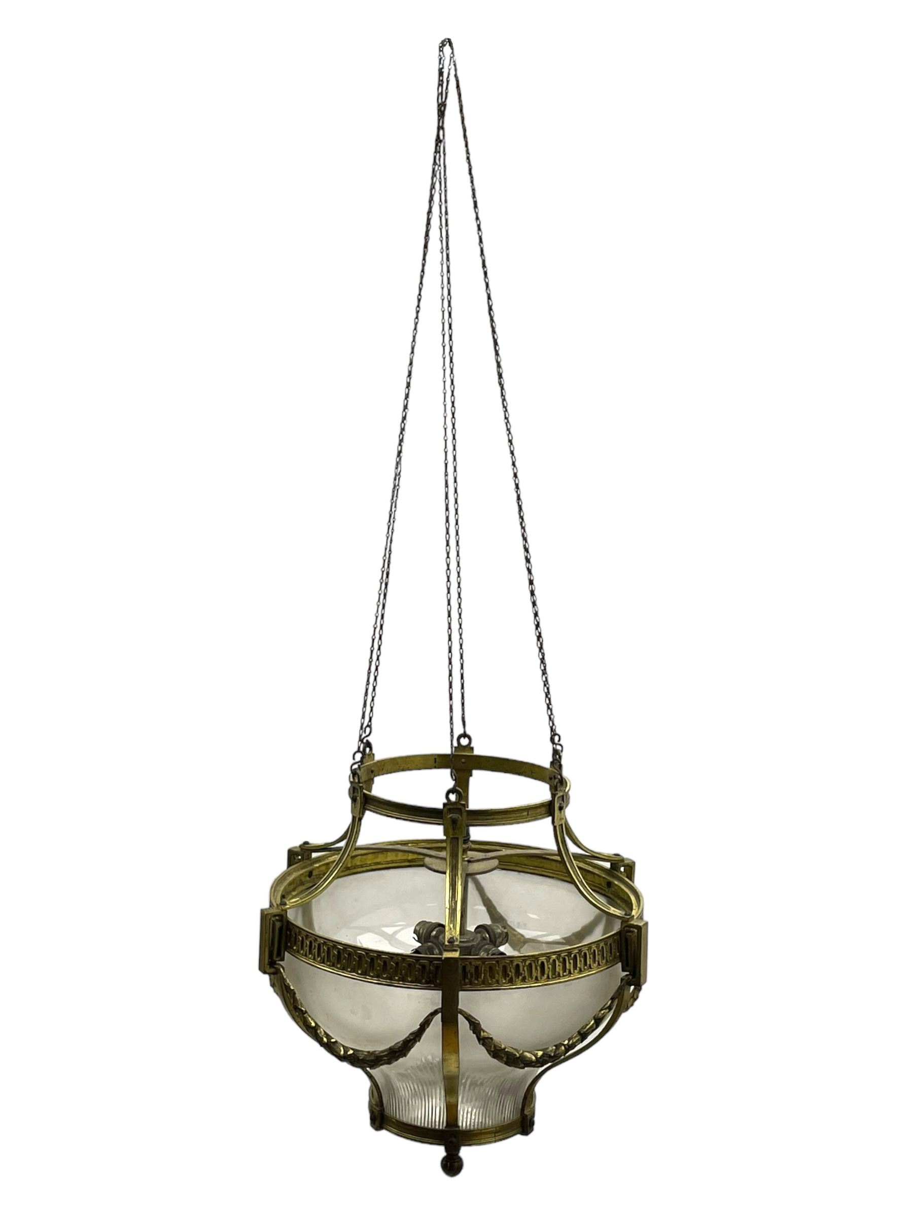 Edwardian brass ceiling light of circular bulbous form, moulded upper band over a guilloche cast central band united by shaped strapping, decorated with fruiting foliage festoons, fitted with frosted and vertical bevelled glass bowl, acanthus cast finial 