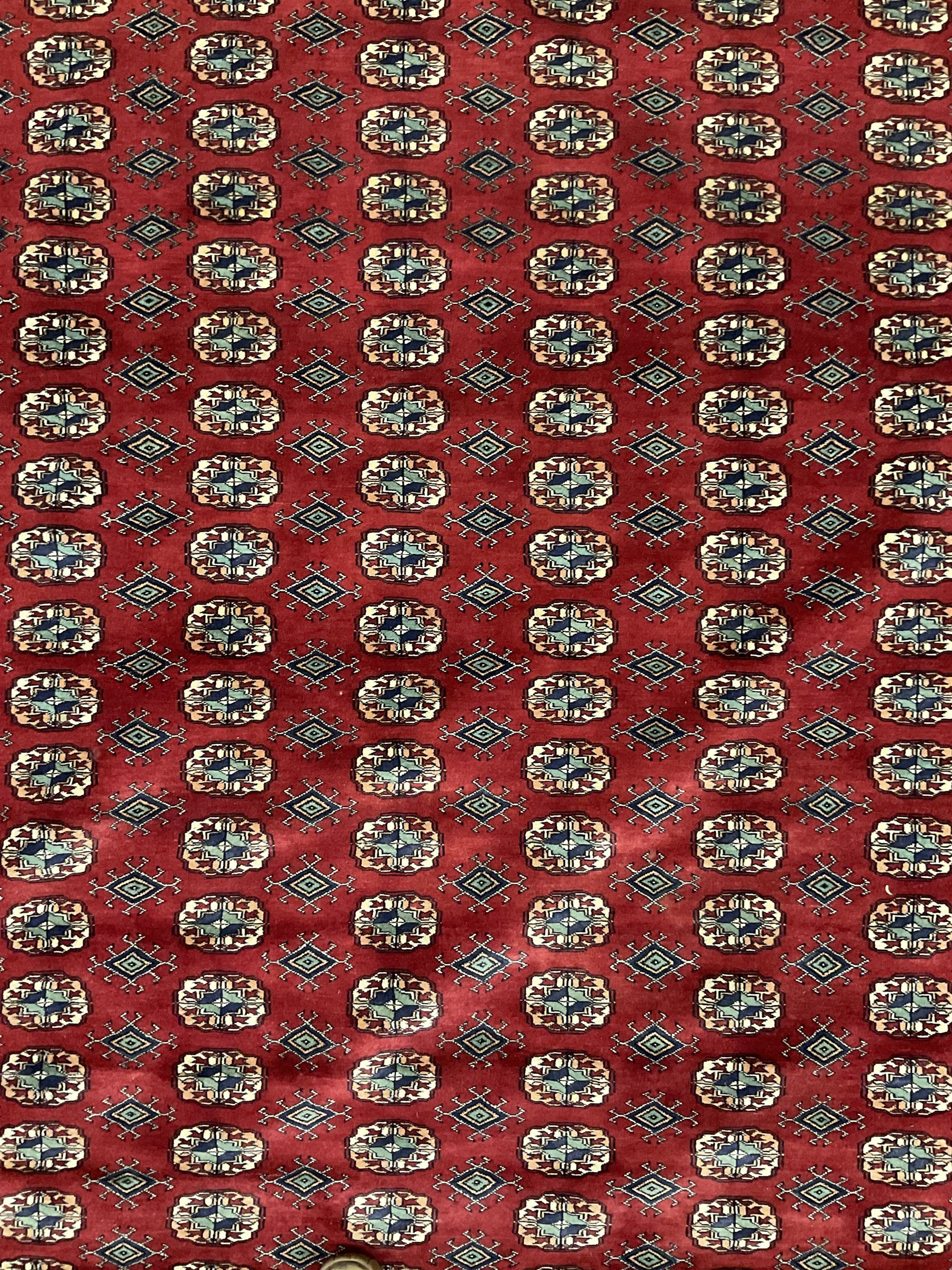 Large Persian Bokhara red ground carpet, the field decorated with eight rows of Gul motifs, wide multi-band borders decorated with repeating geometric motifs