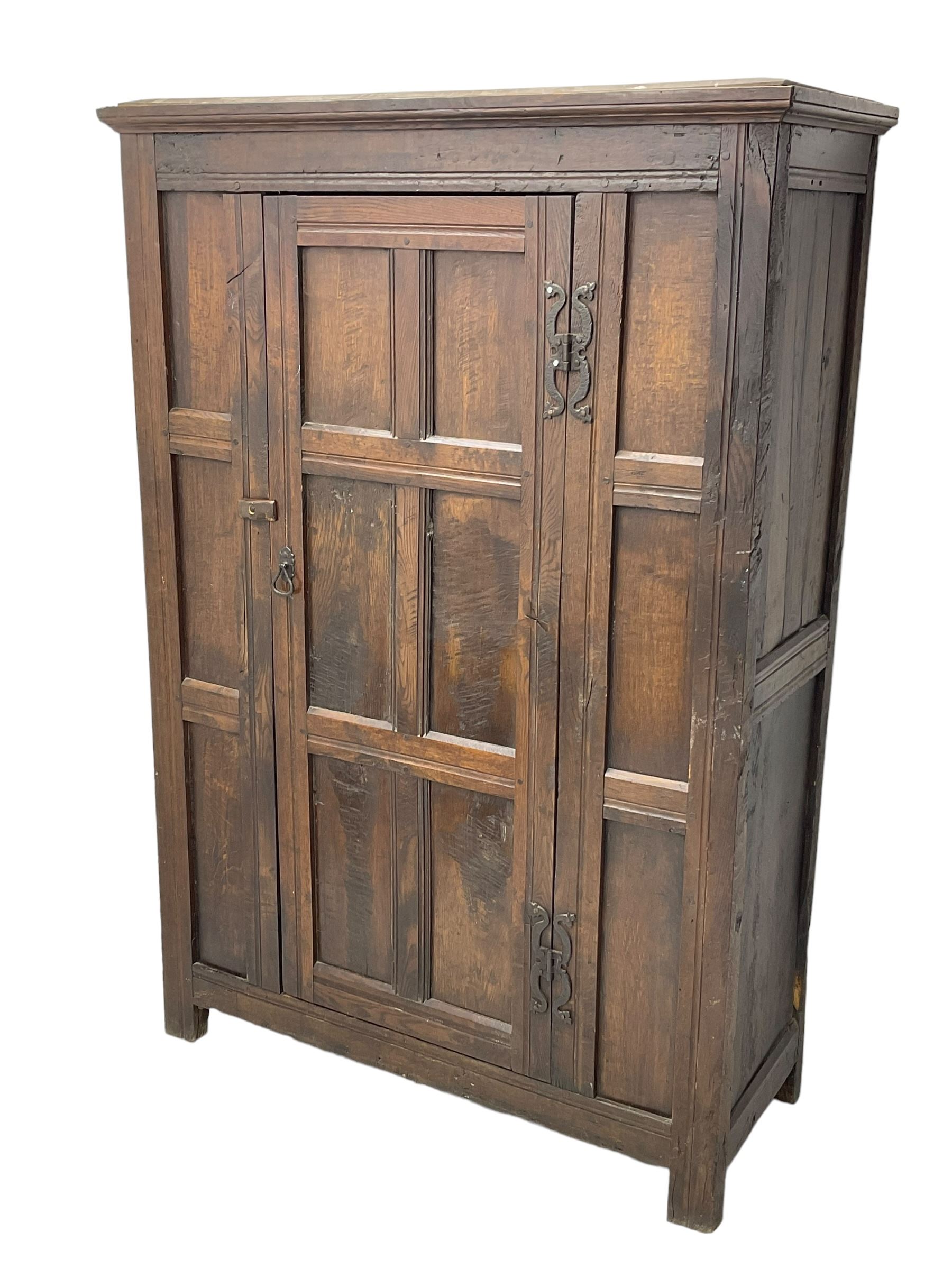 17th century and later oak hall cupboard, panelled front and sides with moulded frame, enclosed by single door with wrought metal hinges and handle, the interior fitted with hooks, on stile supports 