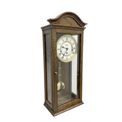 Commiti of London -  three train spring driven 8-day wall clock in an oak case, with a fully glazed door and curved pediment, two part dial with Roman numerals, spade hands and gridiron pendulum, rack movement chiming the hours and quarters on 5 gong rods. With key.