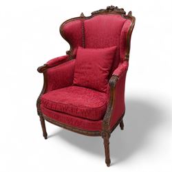 Late 19th century walnut framed fauteuil armchair, arched cresting rail carved with musical instruments and extending floral decoration, curved wing back with moulded and bead carved frame, upholstered in crimson fabric with repeating foliate pattern, acanthus carved arm terminals over acanthus and ribbon carved arm supports, the seat rail carved with fruiting foliage band, on turned and stop-fluted feet 