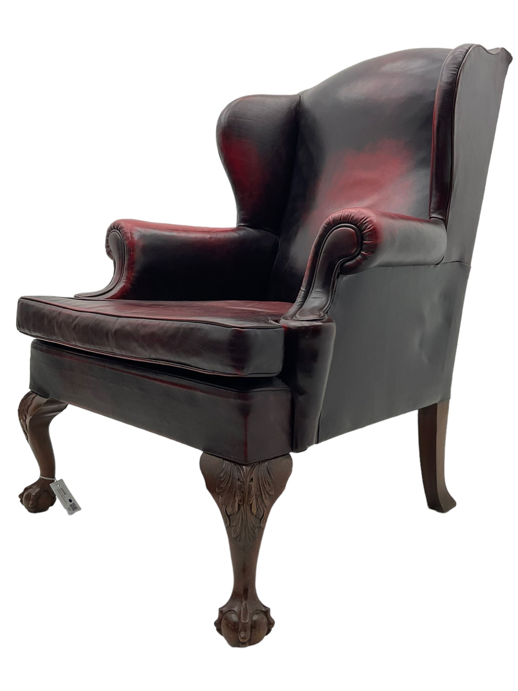 Georgian design hardwood-framed wingback armchair, upholstered in red leather, loose seat cushion and rolled arms, on acanthus carved ball and claw front feet 