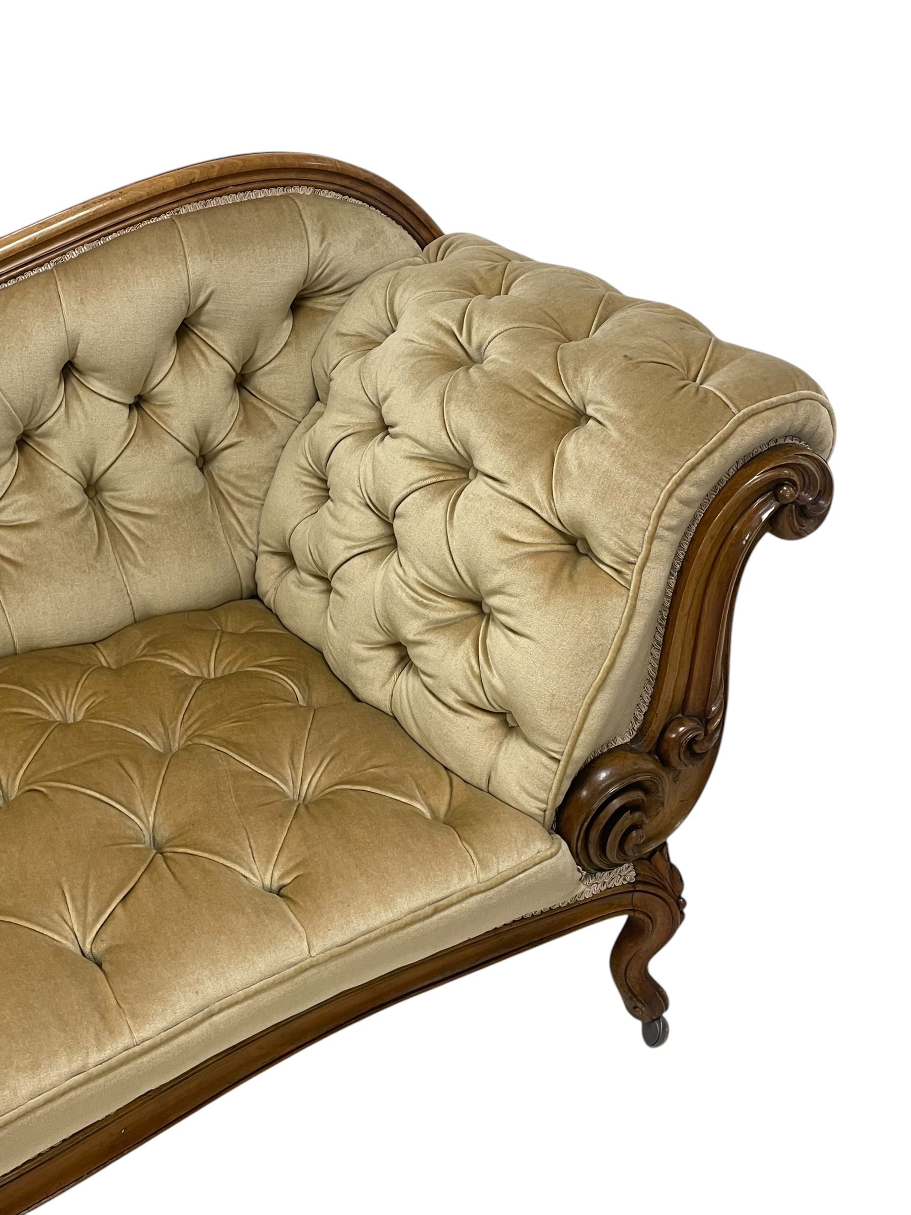 19th century walnut framed chaise longue, shaped back over scrolled arms decorated with moulded curling acanthus carvings, upholstered in deep buttoned champagne fabric, raised on cabriole supports with applied floral carved decoration, on castors