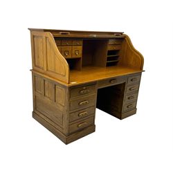 Early 20th century oak tambour roll-top desk, the top with fitted interior including drawers, pigeonholes and compartments, the twin pedestals fitted with four drawers with carved handles, supported by plinth base 