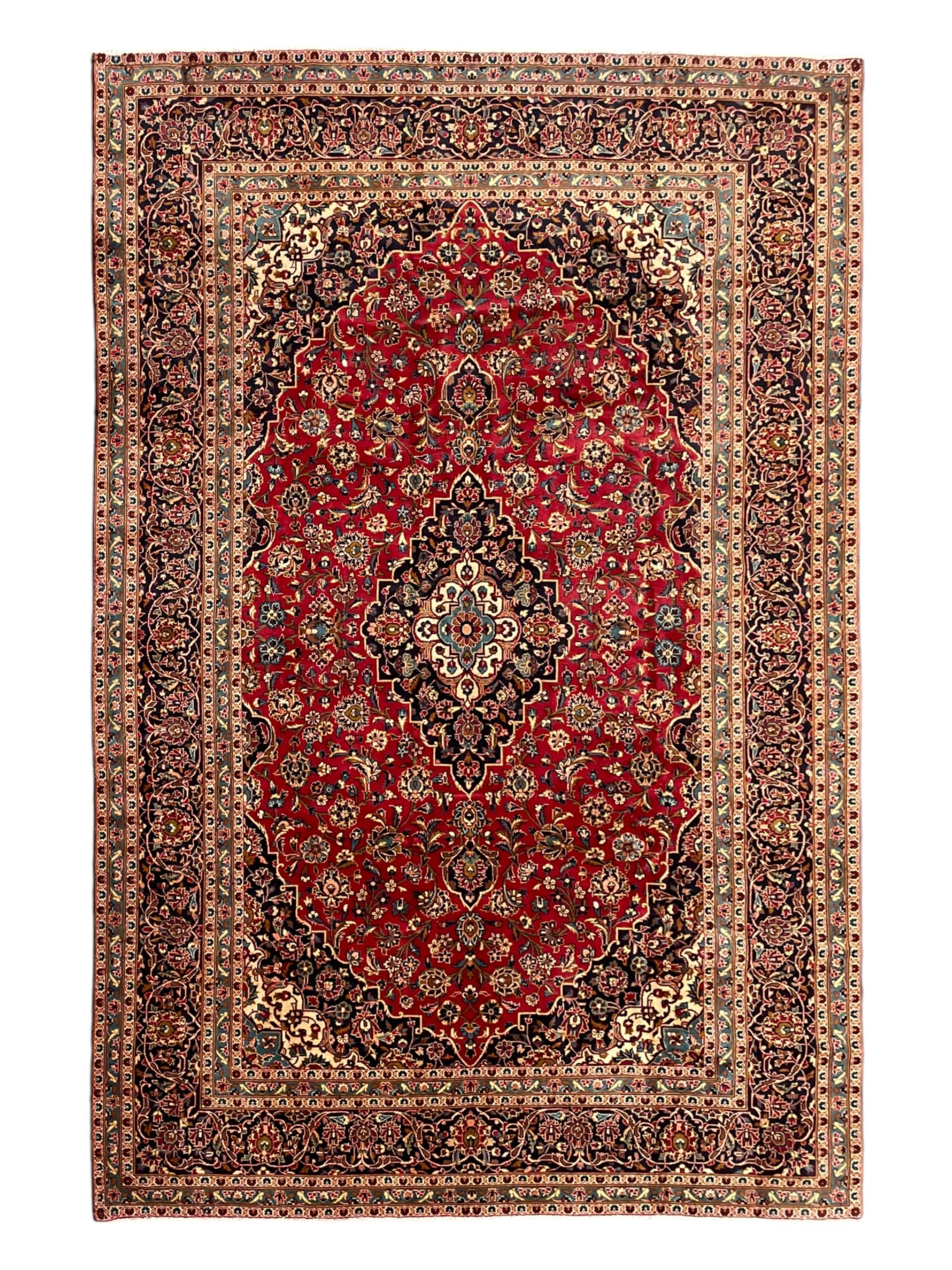 Persian Kashan crimson ground carpet, floral pattern pole medallion surrounded by trailing branches with foliate motifs and palmettes, scrolling border decorated with stylised plant motifs, within multiple guard stripes