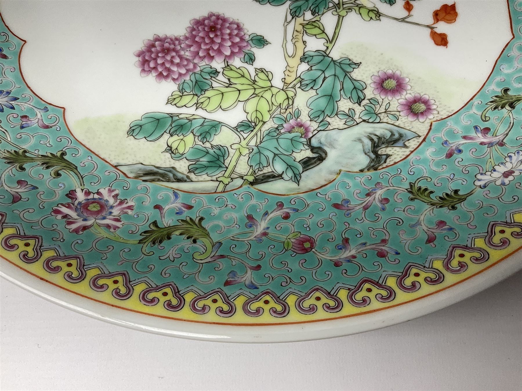 Pair of mid 20th century Chinese Qianlong Nian Zhi Famille Rose chargers, each decorated with two red crested birds perched upon a branch above blossoming pink and yellow peonies and chrysanthemums, within a turquoise border decorated with stylised flowers and scrolls, and yellow outer border, each with Qianlong Nian Zhi mark beneath, D33cm