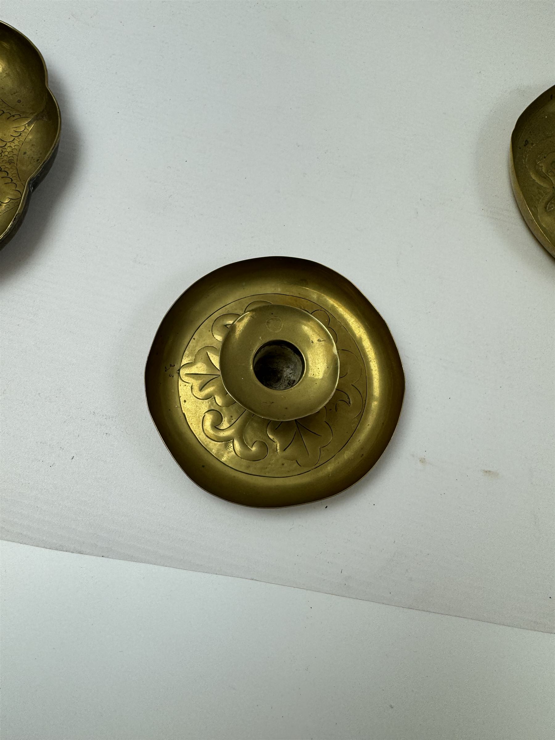 Three Arts & Crafts brass chambersticks/candlesticks, to include a small Keswick School of Industrial Arts example, with repousse leaf decoration, stamped KSIA, a chamberstick with Art Nouveau style decoration to drip pan and blue enamel roundel inset into the loop handle and a larger candlestick, with shaped rim and sconce, repousse decoration and lightly hammered finish, largest D18cm