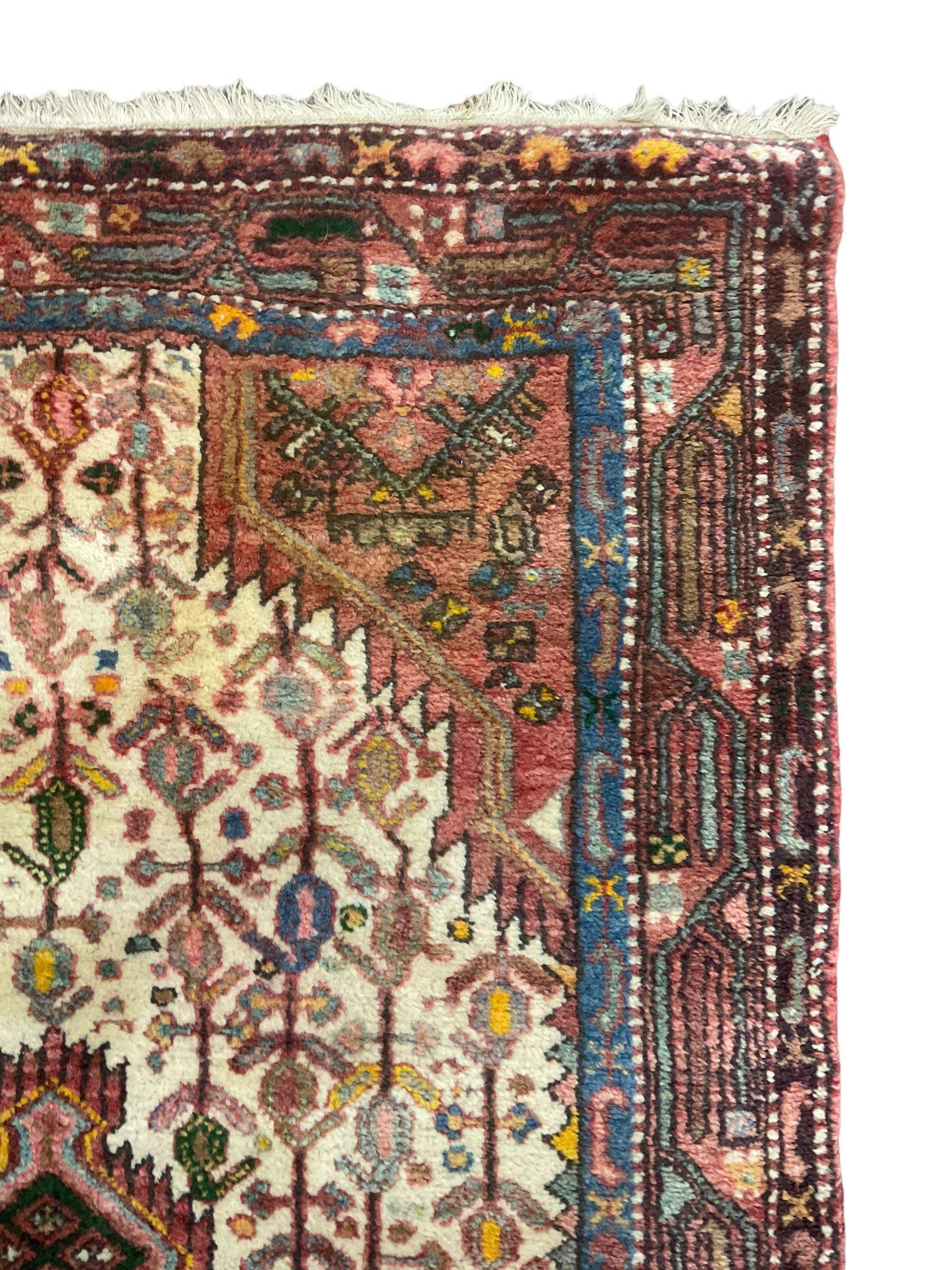 Small Persian rug, ivory and pale red ground, decorated with central medallion within a field of trailing Boteh motifs, geometric design guarded border