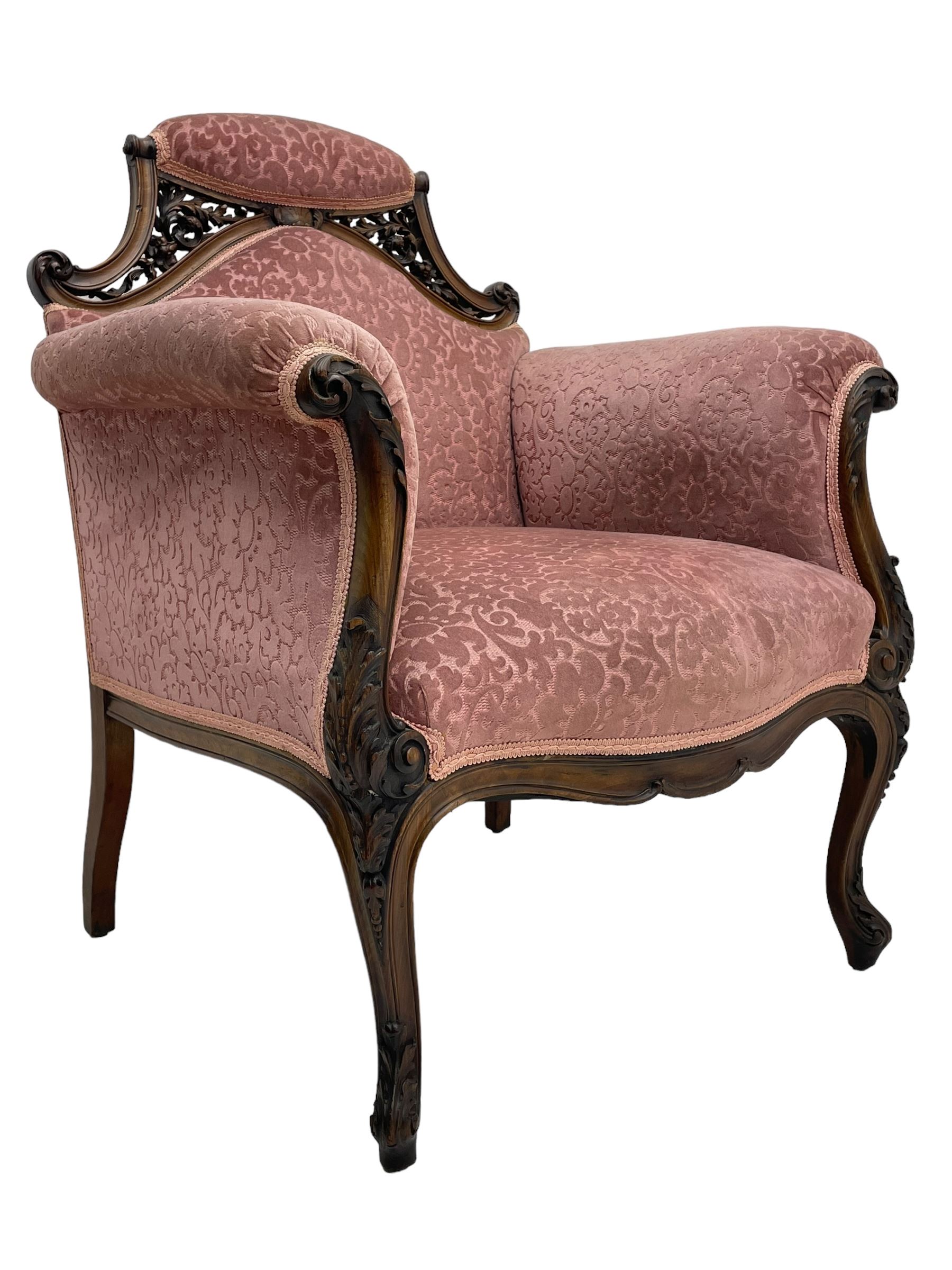 Late 19th century carved walnut framed armchair, the upper spandrels pierced and carved with curled acanthus leaves, upholstered in pink foliate pattern fabric, acanthus leaf carved and scrolled arm facias terminating to cabriole supports, leaf carved terminals 