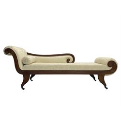 Regency design mahogany chaise longue, scrolled arms with carved rosette details, upholstered in cream damask fabric with bolster cushion, reeded frame supported by turned legs on brass castors