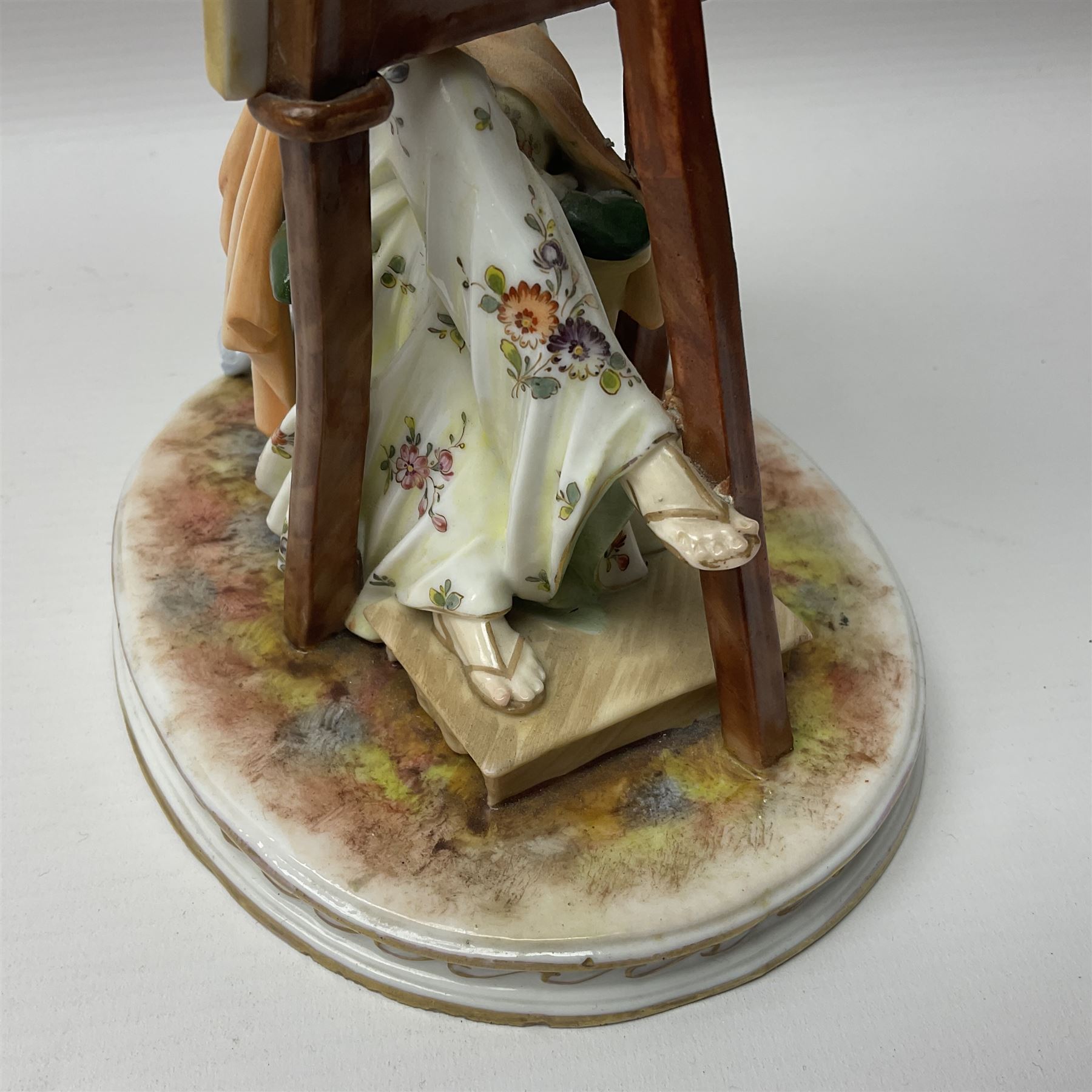 Pair of late 19th/early 20th century Naples figures modelled engaged in the arts, the first example modelled as a female figure seated before an easel, painting a figural scene, the second modelled as a female figure seated before a bust with scultping tools in hand, each upon an oval base with naturalistic painted ground, each with blue crowned N mark beneath, each approximately H16cm, including base L15xm
