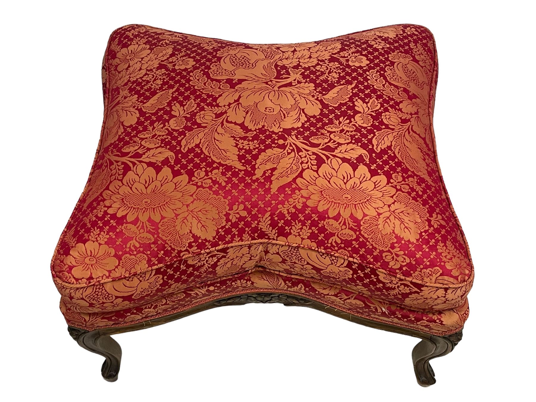 Late 20th century French design stained beech framed armchair and matching stool - the armchair with shaped and moulded frame carved with flower heads and foliage, upholstered in silk red and gold ground fabric with floral pattern, on scroll carved cabriole feet decorated with flower head carvings (W73cm, H82cm, D75cm); the footstool of concaved rectangular form with moulded frame carved with flower heads, upholstered loose cushion, on cabriole feet (70cm x 64cm, H48cm)