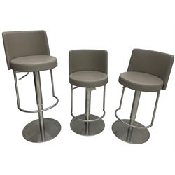 Three contemporary polished metal adjustable Monza bar stools, with taupe faux leather upholstered seats, supported by a brushed stainless steel pedestal base with integrated footrests