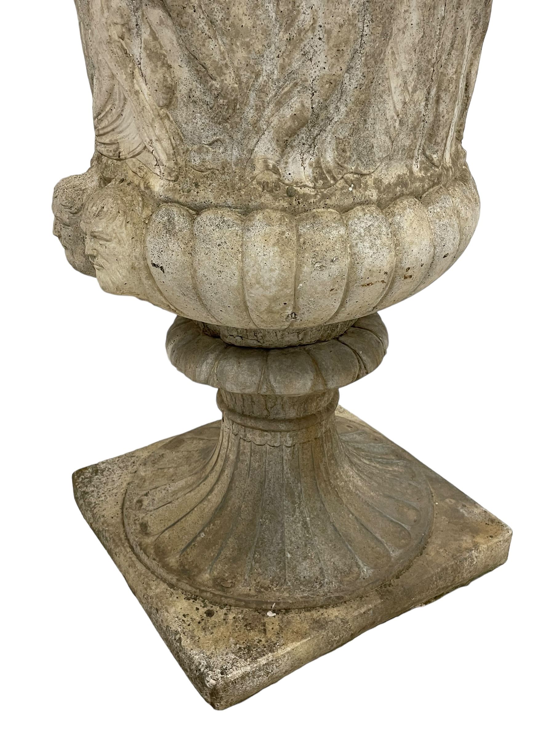 Cast stone Campana shaped urn, decorated with festival scenes over gadrooned underbelly, circular foot on square base