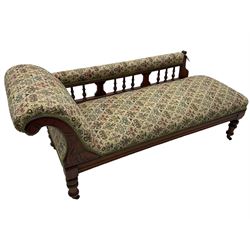 Late 19th century walnut framed chaise longue, upholstered in floral pattern fabric, rolled back rest and turned balustrade back, on turned feet with brass and ceramic castors 