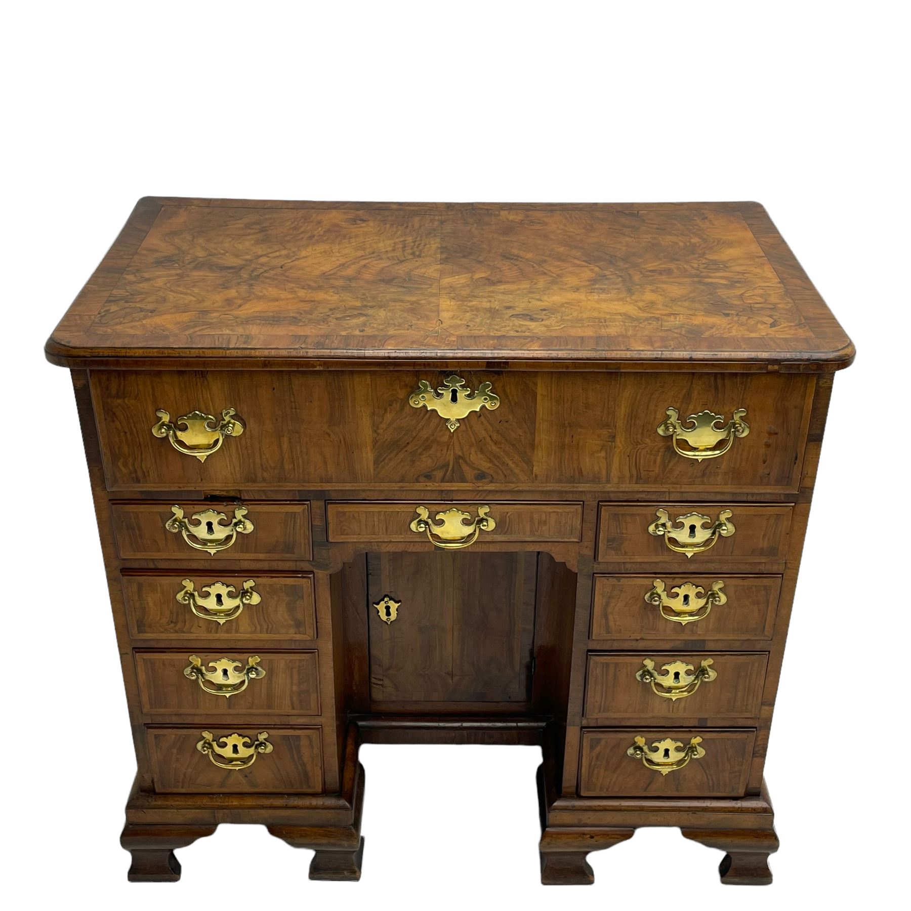 Early 18th century Queen Anne figured walnut kneehole desk with secretaire drawer, moulded and book matched top with walnut band, the top drawer with fall front enclosing small drawers and pigeon holes, fitted with nine drawers and central recessed cupboard, on ogee bracket feet