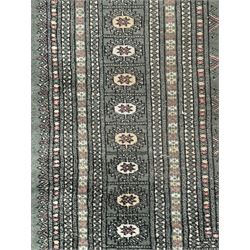 Pakistani Bokhara green ground rug, the field decorated with rows of repeating gul motifs, the main border featuring a series of smaller gul designs and geometric patterns, framed by multiple guard stripes