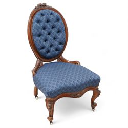 Victorian carved walnut framed nursing chair, the cresting carved with flower heads and extending foliage, upholstered in buttoned blue fabric with repeating pattern, on floral carved cabriole feet