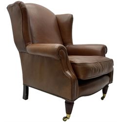 Georgian design wingback armchair, upholstered in brown leather with stud band and piping, turned and fluted front feet on brass cups and castors