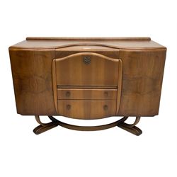 Beautility - mid-20th century walnut sideboard, fall-front with sliding top enclosing mirror interior, fitted with two drawers and flanking cupboards, on sledge feet with curved stretchers 