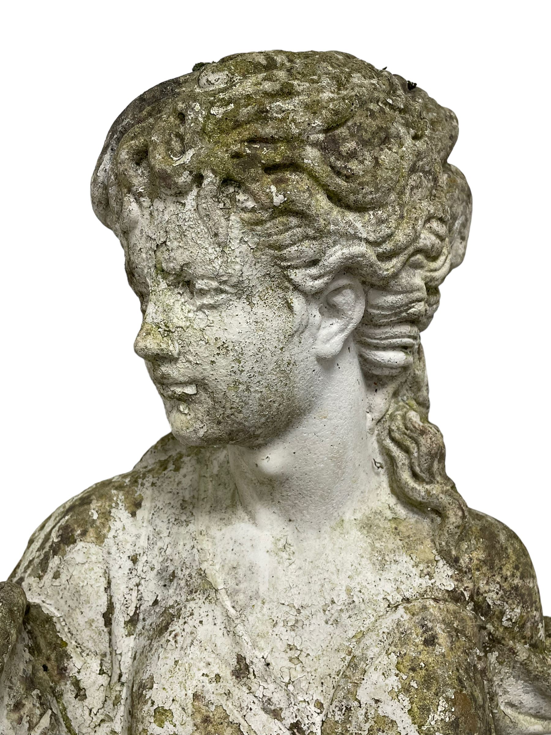 Weathered and painted cast stone garden statue, in the form of an Italian maiden carrying baskets with gathered flora and berries, on a shaped ovoid base