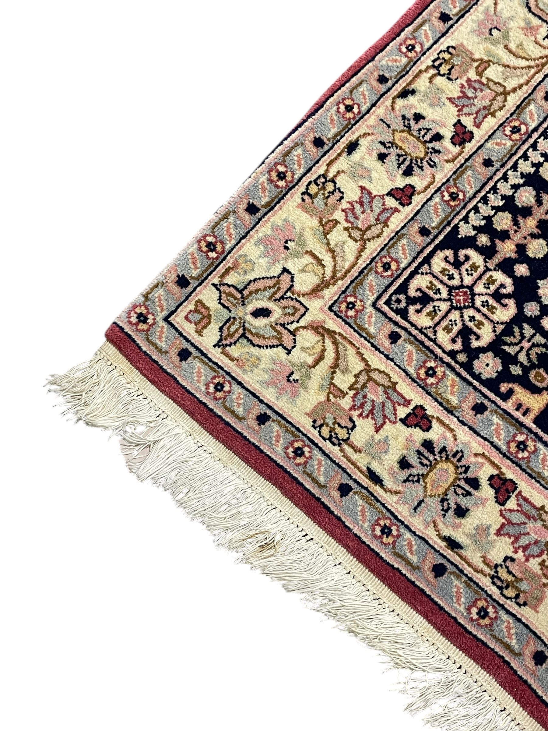 Persian design crimson ground rug, the field decorated with tree of life and floral motifs, enclosed by indigo spandrels with stylised flower head decoration, repeating scrolling border 