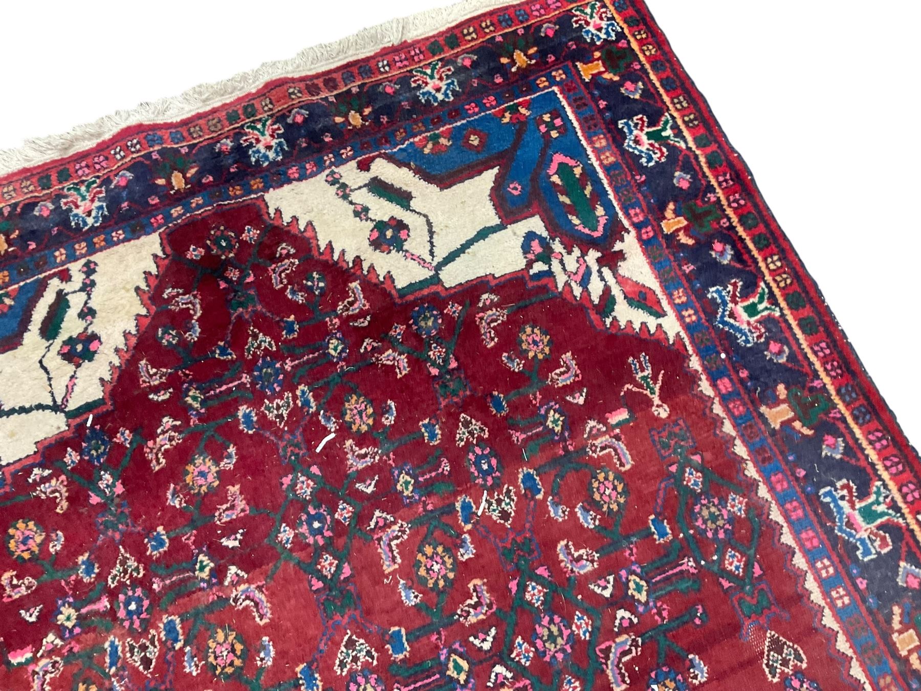 Persian Herati crimson ground rug, the busy field decorated with a central lozenge medallion surrounded by interlocking Herati motifs, the indigo guard band with repeating palmette and stylised plant motifs