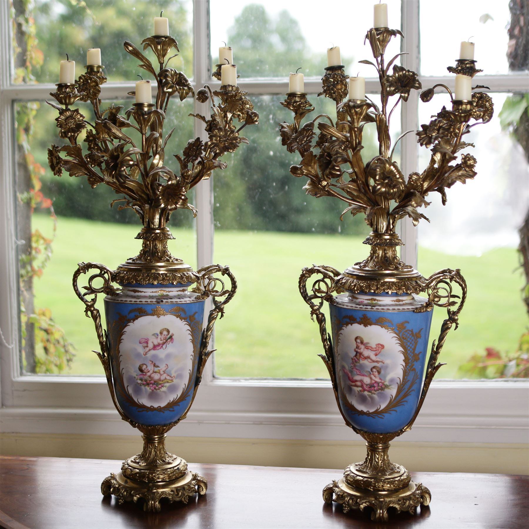 Pair of 19th century Sevres pattern porcelain and ormolu six light candelabra, each with branches cast as lilies, carnations etc, the two handled vase shaped base with oval panels painted with cherubs amongst flowers on a bleu de ciel surround and raised on an ormolu foliate stem and circular base with scrolling bracket feet H76cm (2)  