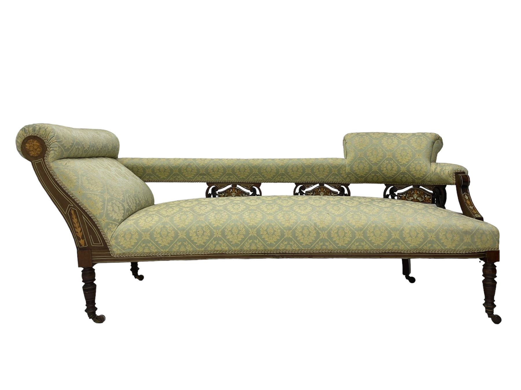 Late Victorian walnut salon settee or chaise lounge, double-ended with rolled back and curved end, upholstered in light aquamarine fabric with raised repeating lozenge pattern, decorated with laurel leaf wreaths and urns, three pierced splats carved with curled leaves, inlaid with dolphins and scrolled foliate motifs in simulated ivory and boxwood, on tapering ring turned supports with brass and ceramic castors (L166, D60, H70cm); together with matching tub-shaped armchair (W61cm, H73cm, D66cm)  