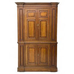 George III and later oak and mahogany banded corner cupboard, moulded cornice over four panelled doors, the door panels inlaid with mahogany bands, projecting square pilasters throughout with applied reeded mouldings, the painted interior fitted with shaped shelves, on moulded plinth base 