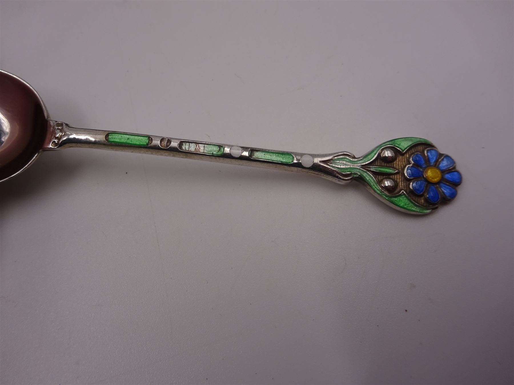 Set of twelve silver coffee spoons, each with enamelled blue flower to terminal and green and white enamel decoration to stem, hallmarked Mappin & Webb Ltd, Birmingham 1934, contained within fitted case