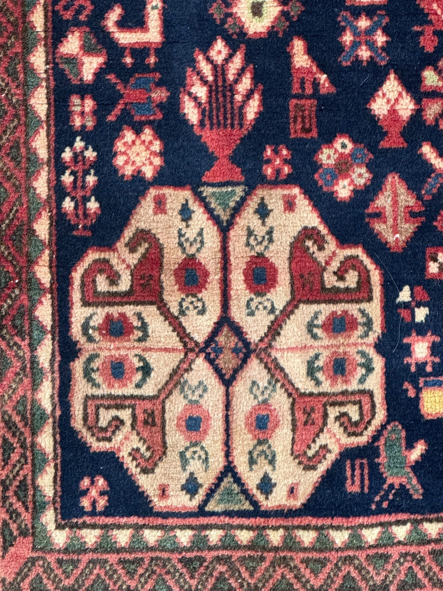 South West Persian Abadeh crimson ground rug, indigo ground with crimson lozenge field, decorated all over with small stylised motifs of flowerheads, hooks, animals and birds, guarded border decorated with trailing leaves and stylised plant motifs 