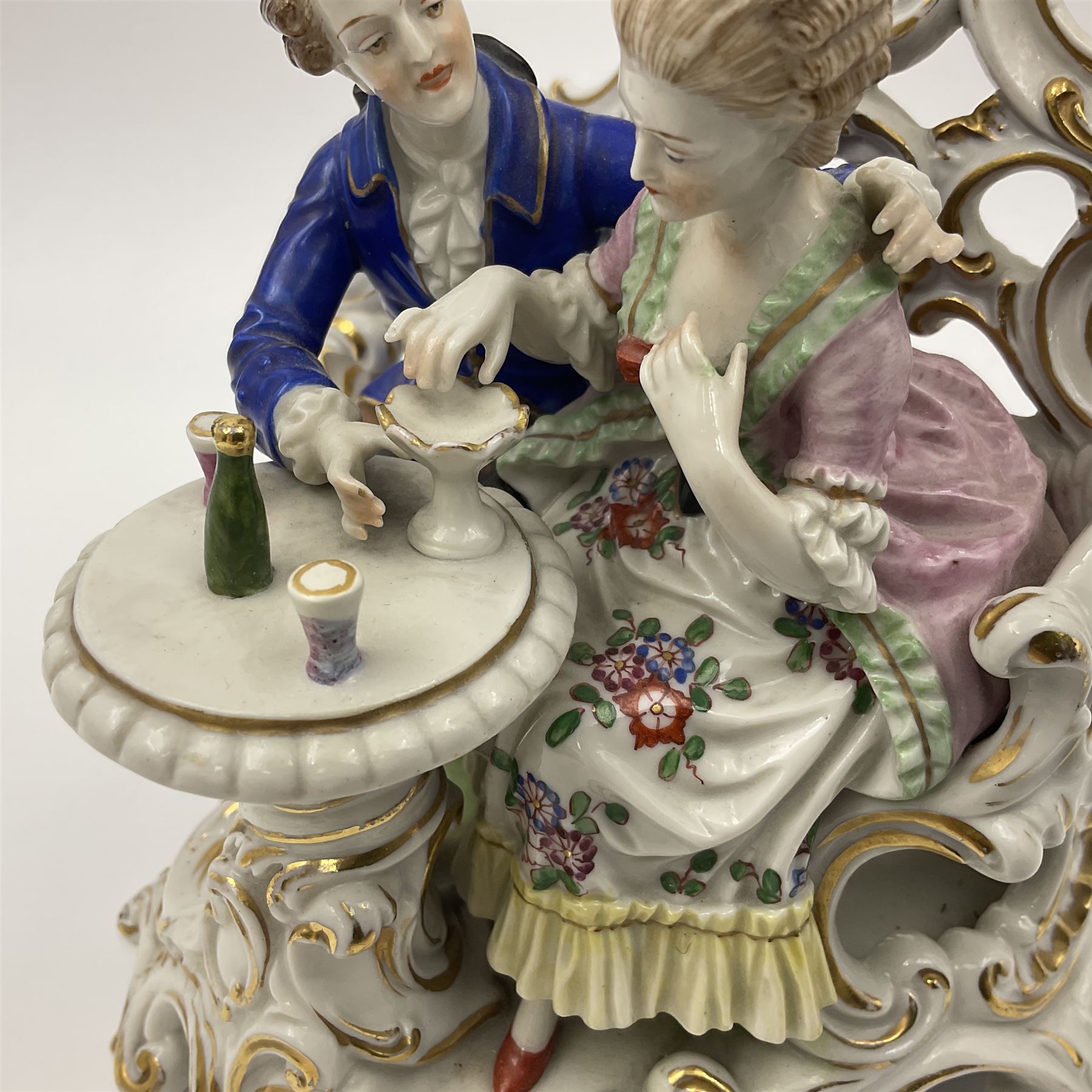 Figure group, probably Volkstedt, modelled as a courting couple seated before a table, the ornate bench and table conforming with and leading from the gilt heightened scrolling base, with blue painted mark beneath, H14.5cm
