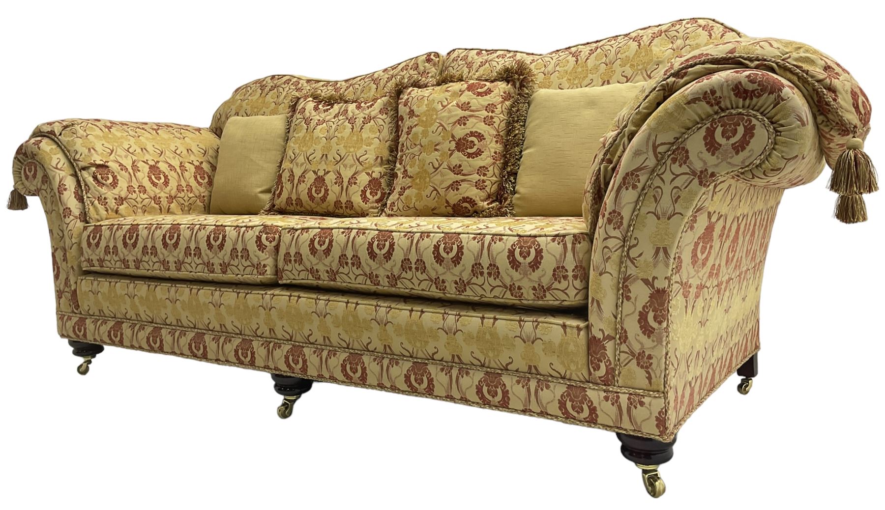 Steed Upholstery Ltd. - 'Lincoln' three-seat sofa upholstered in gold 'Olympia' floral pattern corded and tasselled fabric, together with scatter cushions and arm covers, on turned feet with brass castors