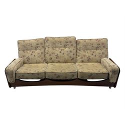 Mid-20th century three-seat sofa with floral patterned upholstery, supported by a sculpted teakwood frame with curved cutout detailing, loose cushioned back and seat, on tubular metal feet