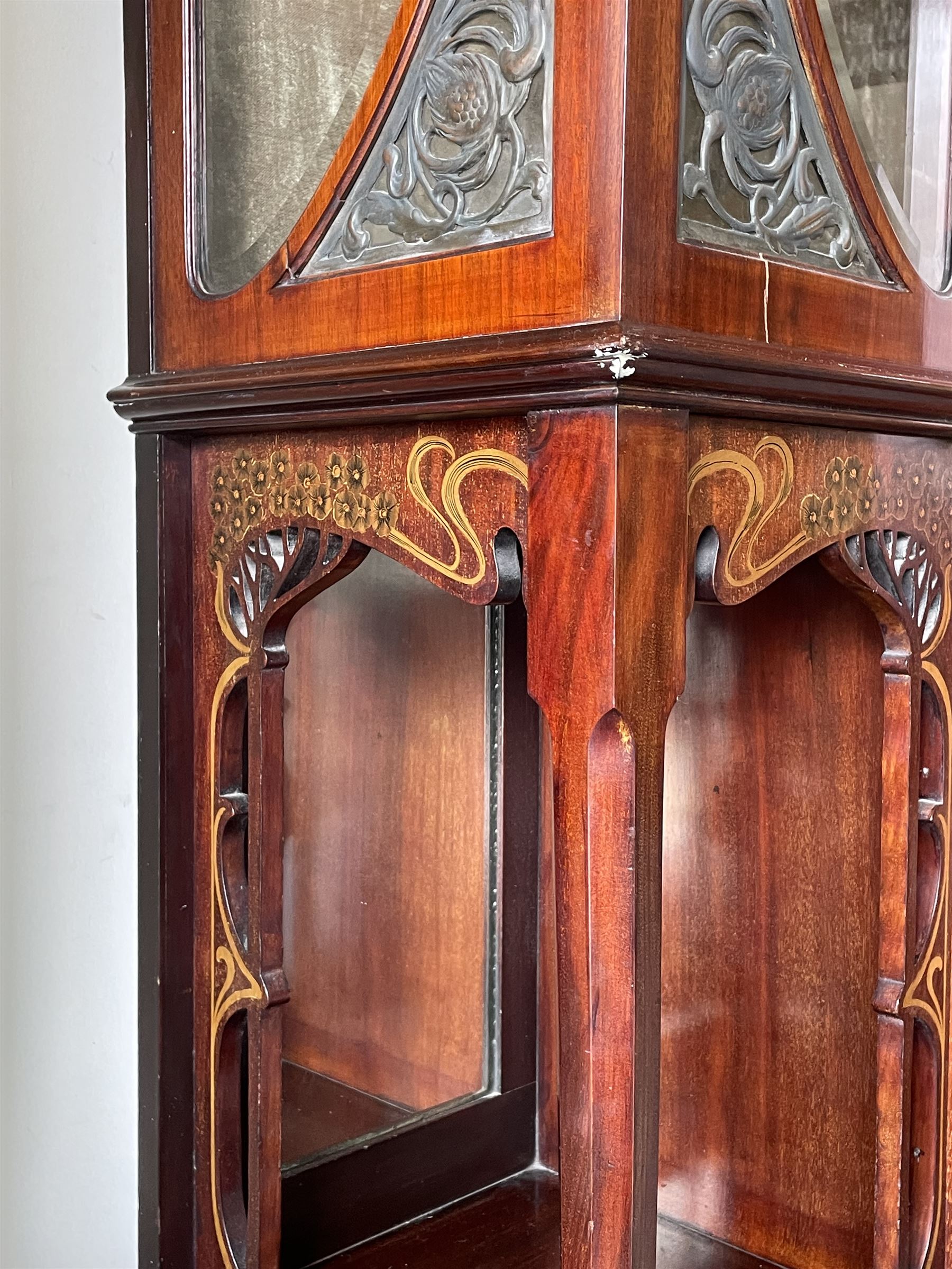 Art Nouveau period inlaid mahogany display cabinet, raised shaped and moulded pediment over projecting moulded cornices, the upper frieze inlaid with trailing branches and tulips, single astragal and bevel glazed door enclosed velvet lined interior fitted with shelves, flanked by curved glass panes decorated with pierced metal foliate spandrels, lower flanking shelves with mirror backs enclosed within shaped and pierced rails inlaid with flower heads, on tapering octagonal supports terminating to compressed pad feet, the lock stamped 'Salmon Bros, London' 