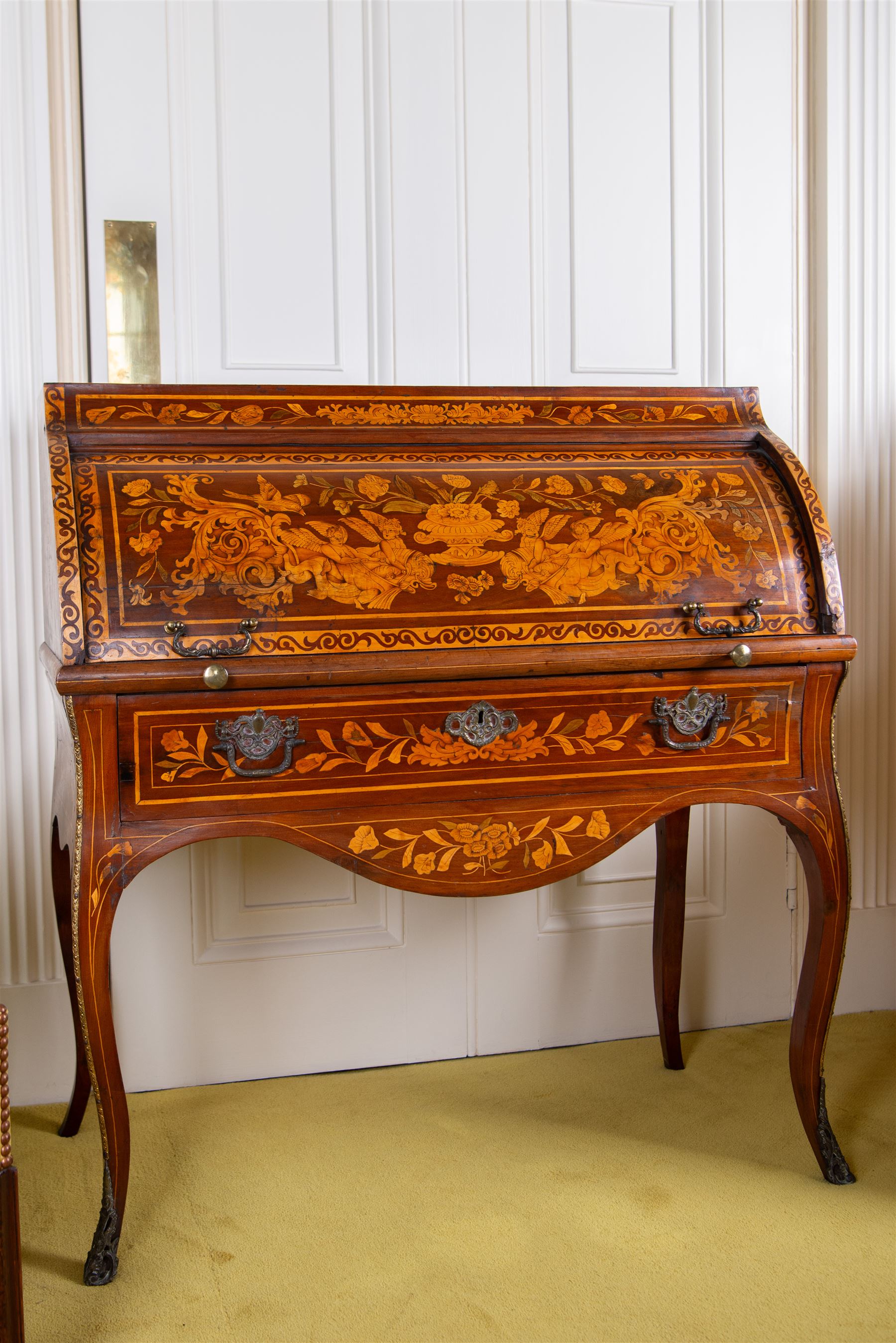 19th century Dutch marquetry cylinder bureau or desk, the cylinder roll inlaid with scrolling acanthus leaves and putti riding dolphins, hook scrolling border, the interior fitted with small drawers, pigeon holes and retractable writing surface, single drawer below inlaid with trailing foliate branches, on cabriole supports with gilt metal mounts