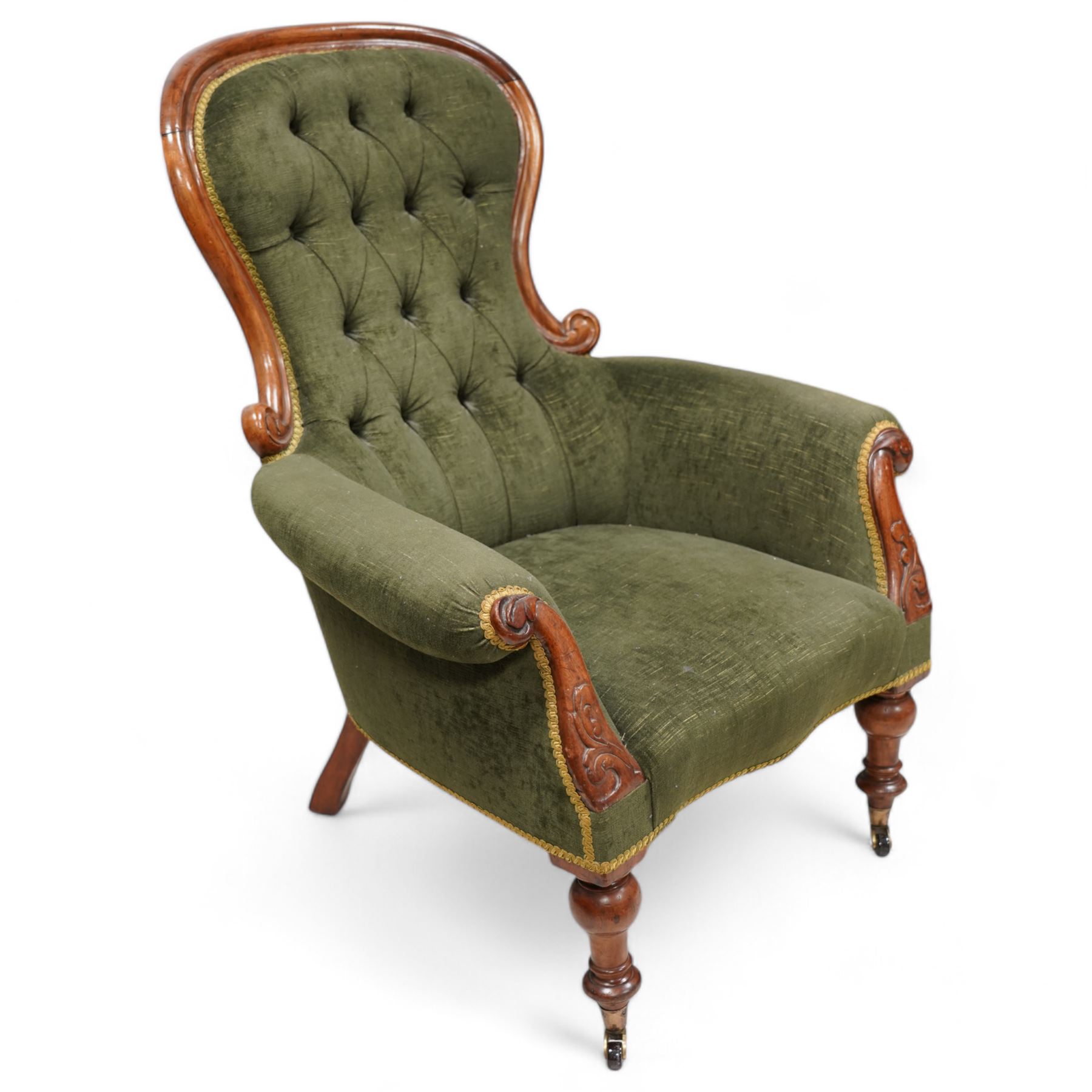 Victorian mahogany spoonback armchair, moulded frame with scroll carved terminals, upholstered in buttoned green fabric, rolled arms with foliage scroll carved facias, on turned front feet with brass cups and castors 