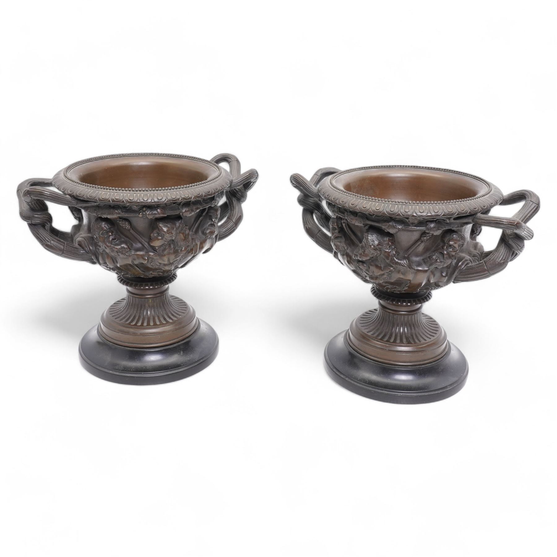 Pair of 19th/ early 20th century bronze 'Warwick' vases, after the antique, of typical form, cast with Bacchic masks and Thyrsus, on a lion pelt-cast ground, with egg and dart and beaded borders and twin reeded bifurcated branch handles, on square marble plinths, H17cm x W20cm