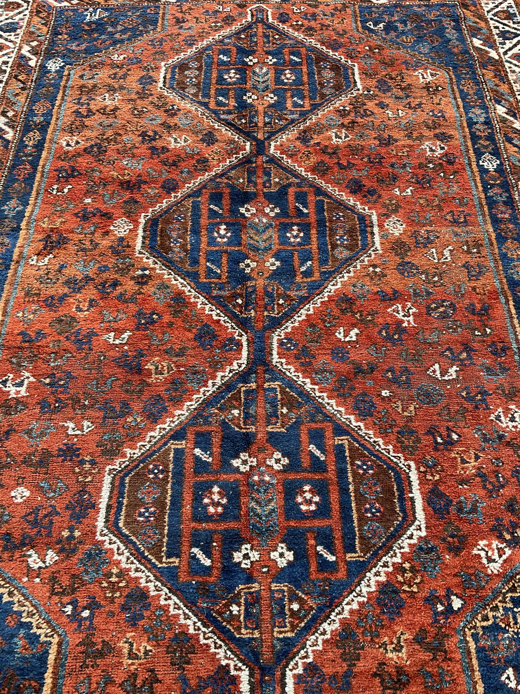 Persian Shiraz crimson ground rug, three connected lozenge medallions on a field decorated with small bird motifs, the main border decorated with repeating geometric motifs, within hooked guard stripes 