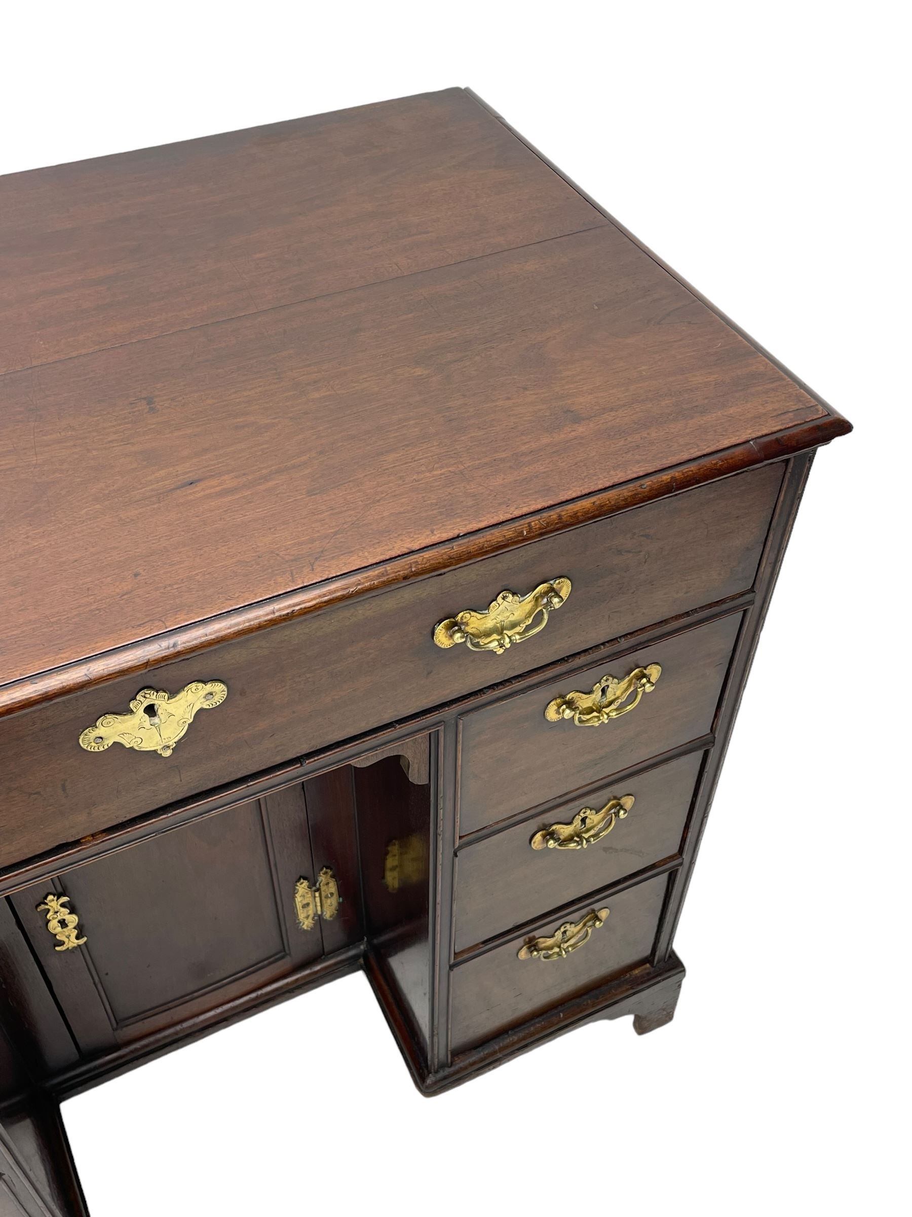 George III mahogany kneehole desk, moulded rectangular top over one long drawer, six short drawers and recessed panelled cupboard, cock-bead moulded frame, fitted with shaped brass handle plates with engraved decoration, on bracket feet 