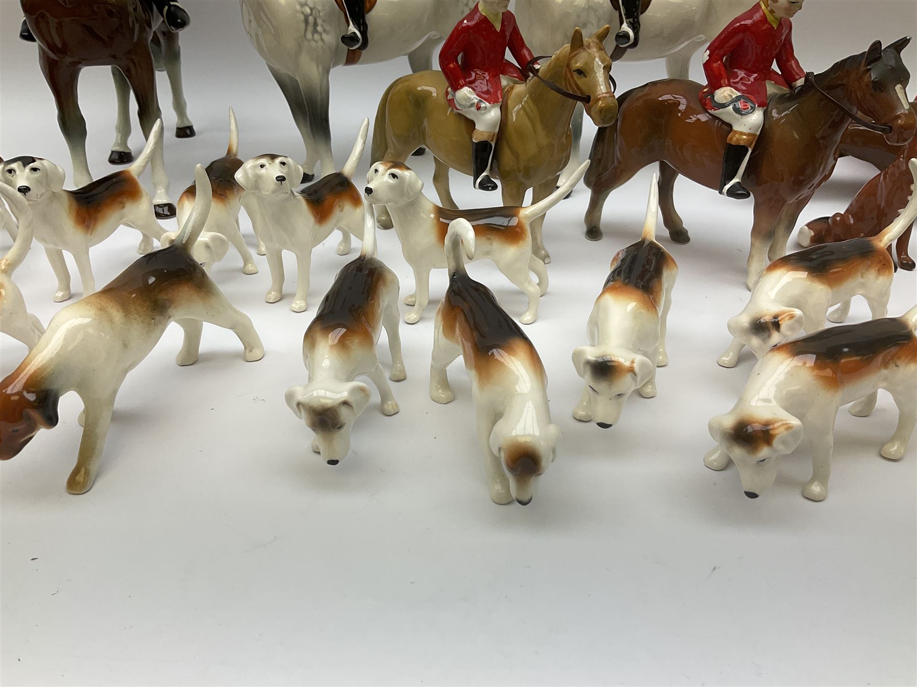 Beswick Hunting Group, comprising: two huntswoman on grey horses, model no 1730, huntsman on a bay horse, model no 1501, a seated fox, model no 1748, eighteen fox hounds and a spaniel, model no 967, all with printed marks beneath, together with three other ceramic huntsman on horseback and two hounds. 