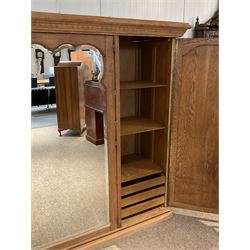 Late 19th century oak triple wardrobe, wide central bevelled mirror door, flanked by two panelled doors each carved with scrolling leaves and flower heads, on moulded skirt base 