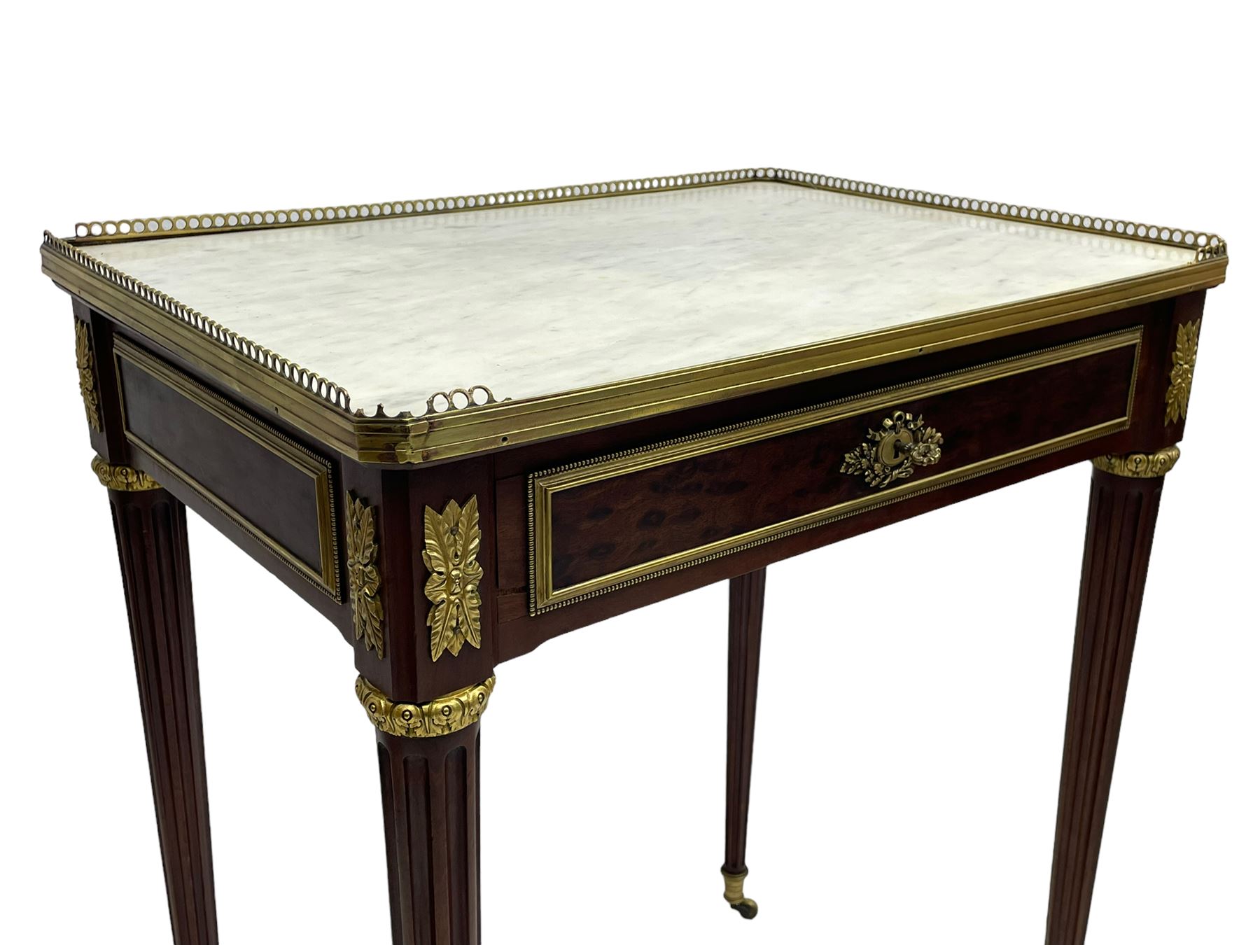 Late 19th century French figured plum pudding mahogany side table, canted rectangular white marble top with raised gilt metal gallery, fitted with a single frieze drawer, central extending floral cast ormolu escutcheon and applied moulded edging, on tapering turned and fluted supports with brass cups and castors, decorated with cast foliate mounts and foliate cast collars 