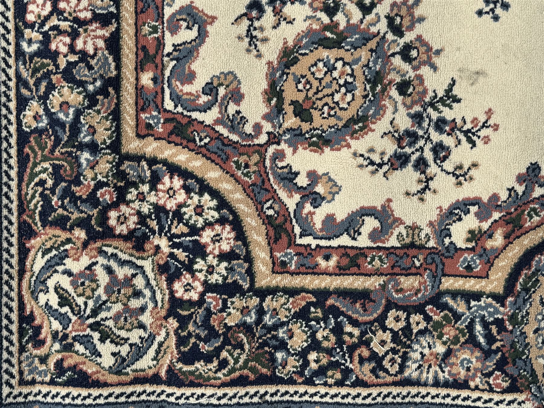 Persian design ivory ground rug, the field decorated with an oval medallion filled with floral motifs and scrolling vines, flanked by floral sprays and corner spandrels with palmette designs, the main border featuring a series of stylised floral patterns against a dark blue ground, enclosed by multiple guard stripes with geometric and floral motifs