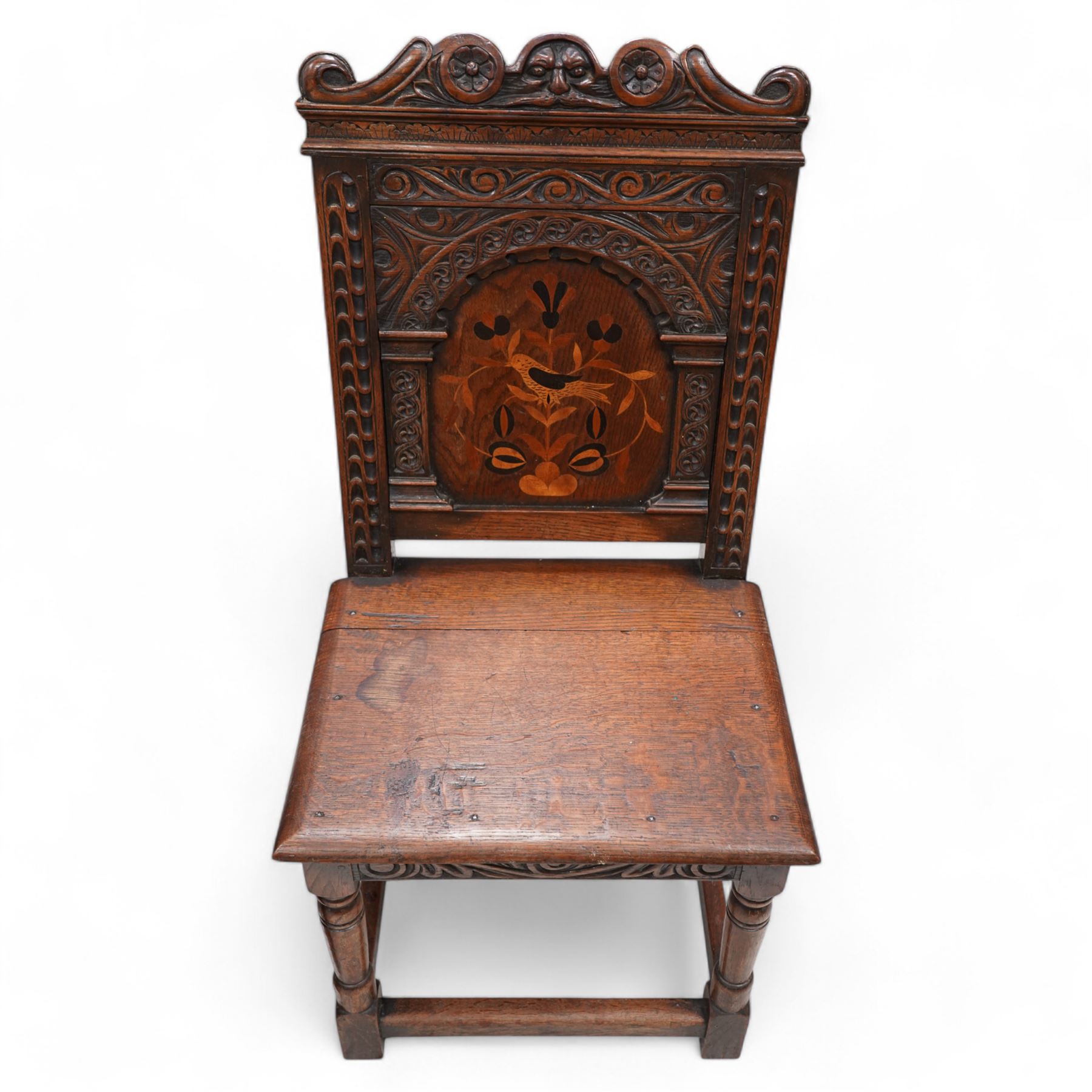 Pair of 19th century Dutch style marquetry oak hall chairs, cresting rail carved with a central green man mask with flanking scrolls, the panelled back inlaid with a bird motif within a guilloche carved arch, panelled seat over scrolling foliate carved apron, on ring turned supports united by box stretcher