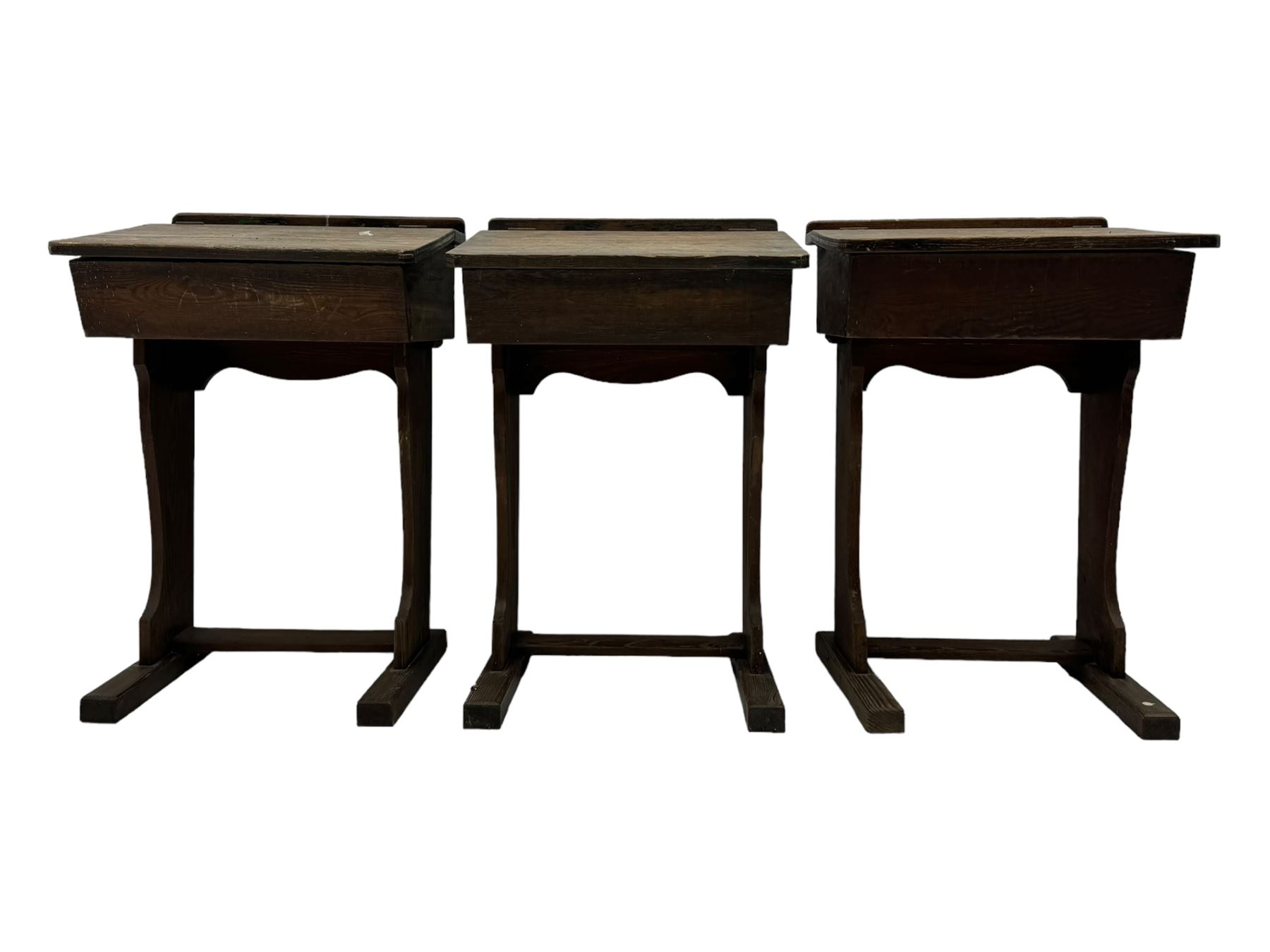 Three pitch pine school desks, each with rectangular lift-top with recessed ink well enclosing storage compartment, on trestle supports joined by stretcher