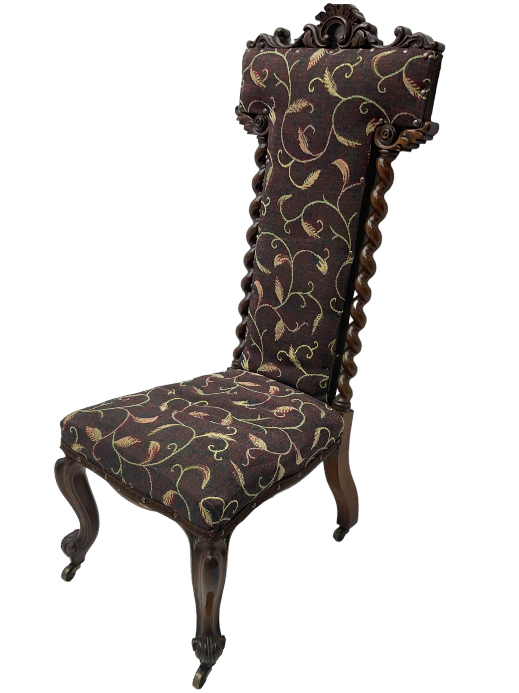 Victorian walnut prie-dieu chair, cresting rail carved with cartouche and extending scrolling foliage, back flanked by spiral turned column uprights, upholstered in foliate patterned fabric, raised on cabriole supports with scroll feet and castors