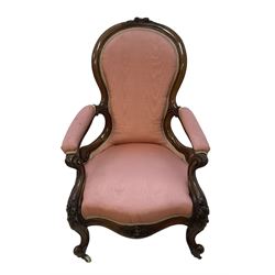 Victorian mahogany framed open armchair, spoon-back and sprung seat upholstered in pink fabric, scrolled arm terminals over serpentine fronted seat decorated with moulded carved floral motifs, cabriole supports with ceramic castors